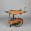 A vintage wooden serving cart or bar table with a light natural wood top, scalloped brass trim, and a lower brass tier, photographed in what appears to be a furniture store or warehouse.