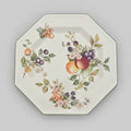 An octagonal white ceramic serving platter decorated with a colorful hand-painted fruit and floral motif, shown on a dark brown wooden surface.