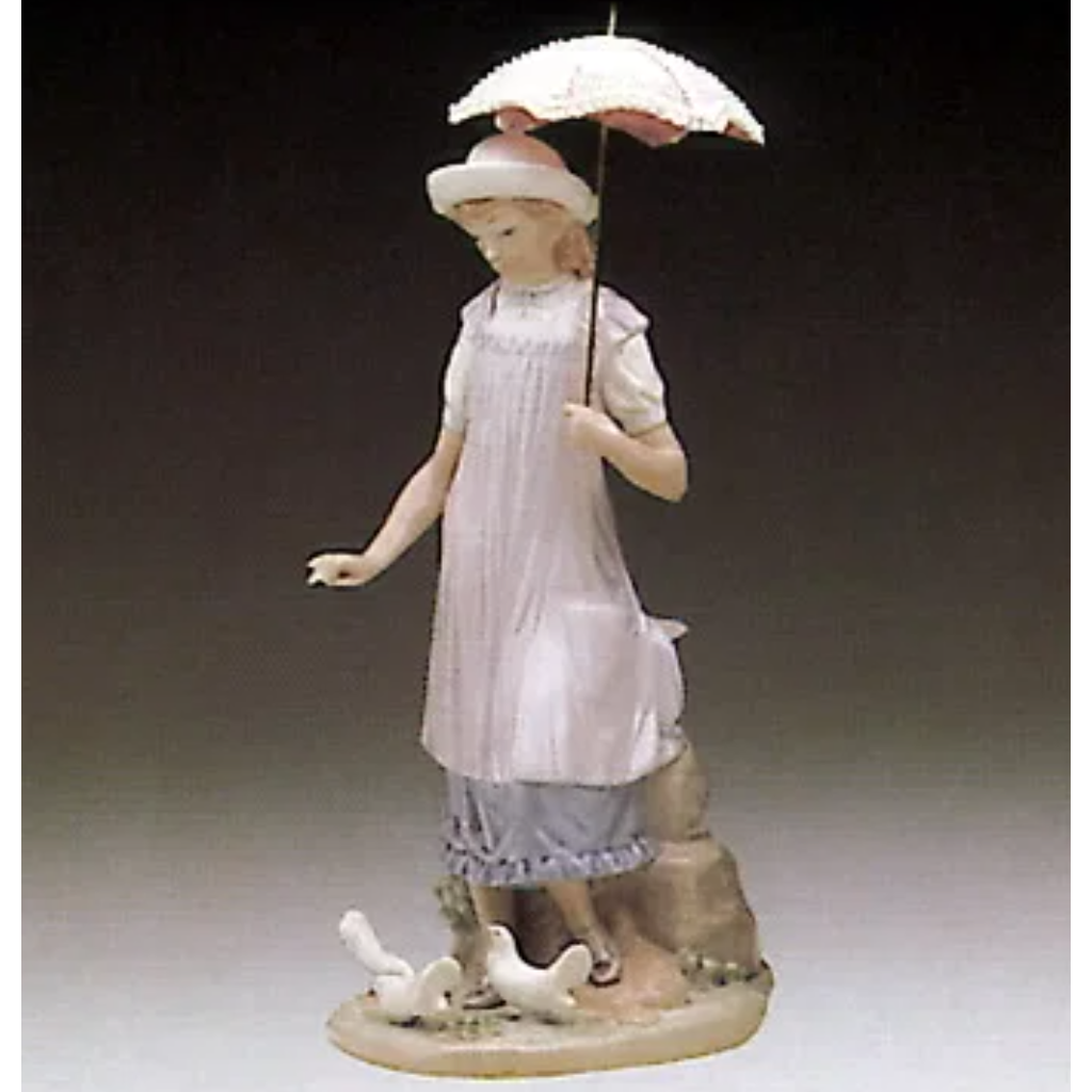 A porcelain figurine of a young girl standing on a base with several white birds at her feet, holding a small parasol. The figurine is dressed in a pale pink and white dress with a white hat.