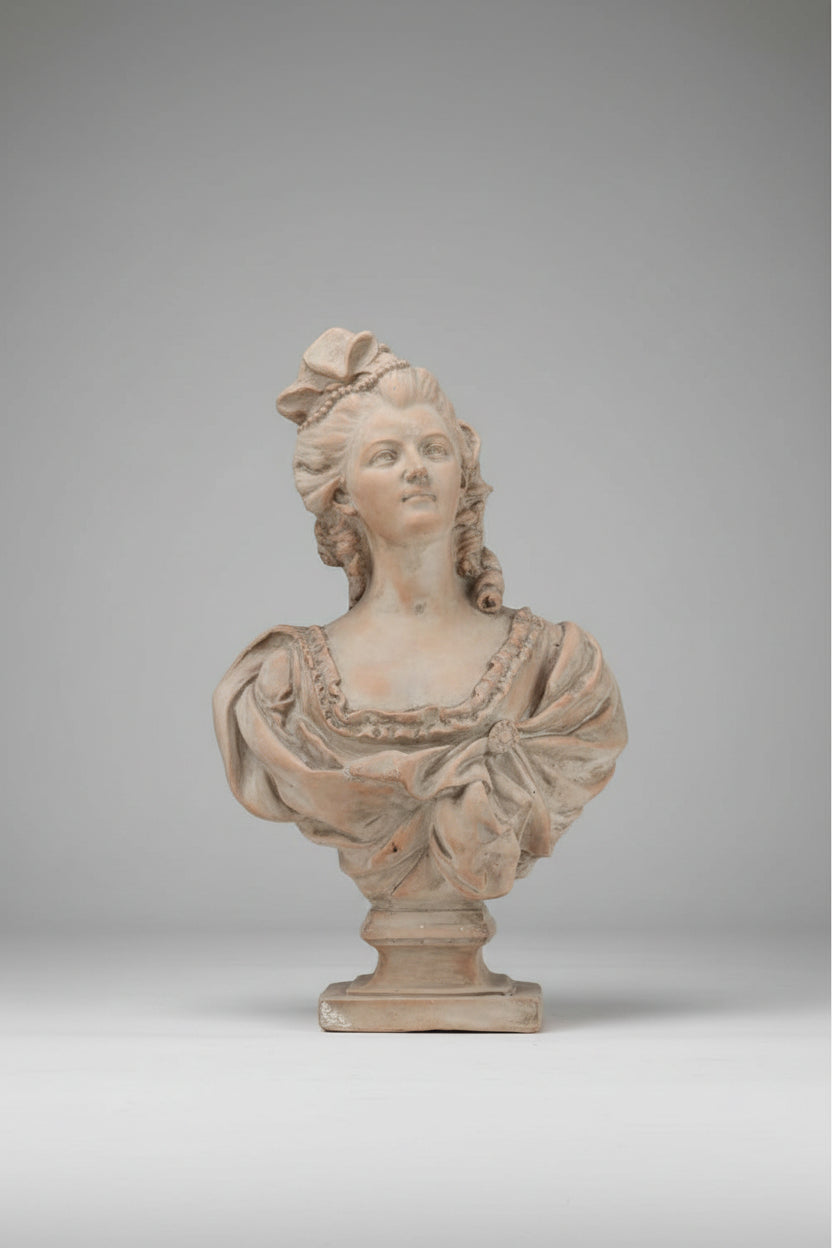 A classical-style terracotta or plaster bust sculpture of a woman with powdered hair and a bow, mounted on a pedestal base against a neutral gray studio background.