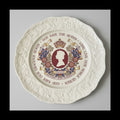 Decorative plate with royal emblem and text on a green fabric background