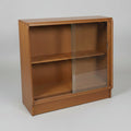 A vintage wooden display case with two glass doors and a base shelf, photographed in what appears to be a furniture store or warehouse.