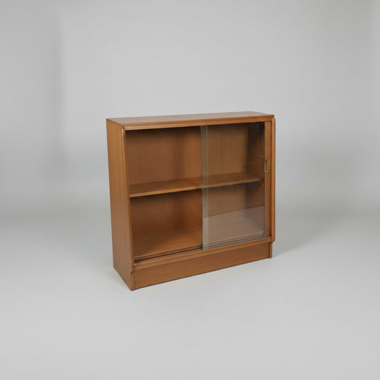 A vintage wooden display case with two glass doors and a base shelf, photographed in what appears to be a furniture store or warehouse.