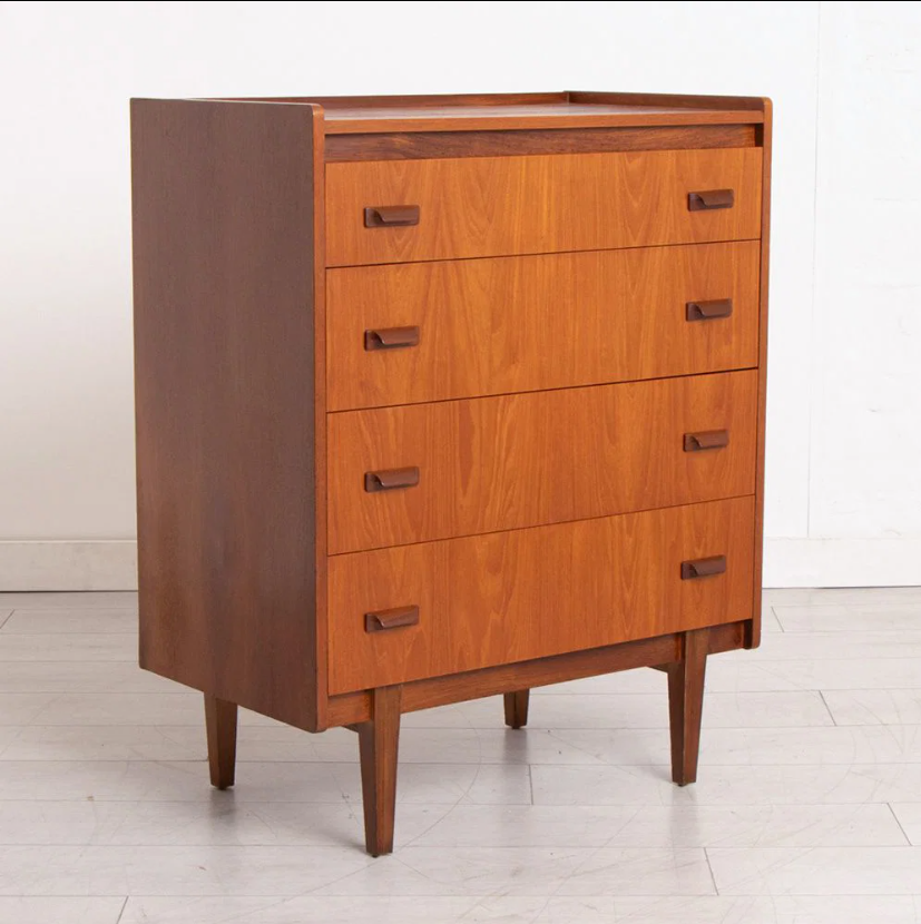 Mid-century modern wooden chest of drawers with five drawers, warm orange-brown wood grain, and dark brown handles, set against a plain white wall and light gray tiled floor.