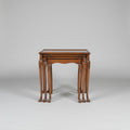 A set of nested wooden nesting tables with carved cabriole-style legs, displayed in a furniture showroom alongside other vintage pieces including a leather armchair and a wooden chest of drawers.