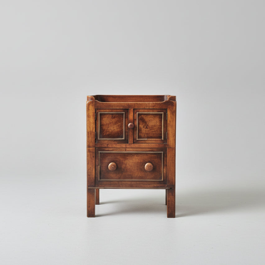 Wooden side table with two drawers on a red patterned rug, with a painting in the background.