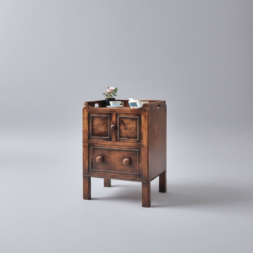 Wooden cabinet with two doors and two drawers on a red patterned rug, with a tapestry on an easel in the background.