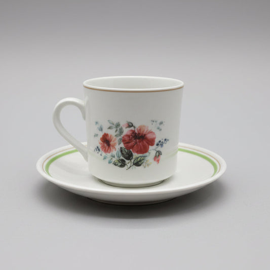 Ceramic mug with floral design on a matching saucer on a decorative tray.