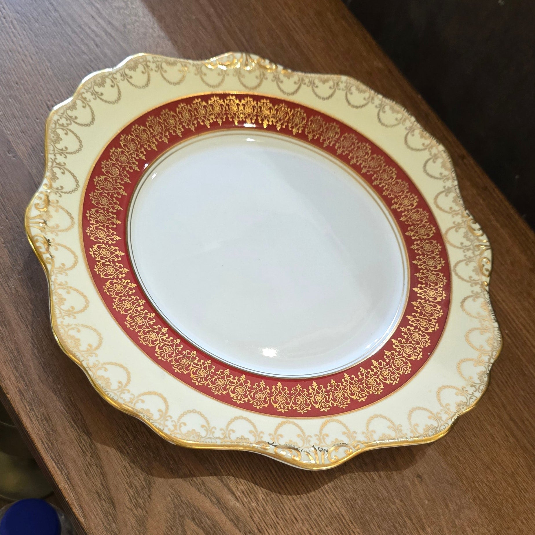 A Royal Stafford fine bone china serving plate with gold and red patterns on the rim, displayed on a wooden surface.