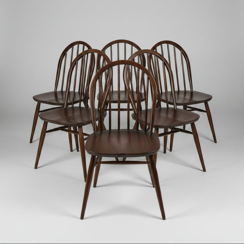 Six dark brown wooden spindle-back dining chairs arranged in a group on a worn reddish-brown floor inside what appears to be a furniture store or warehouse.
