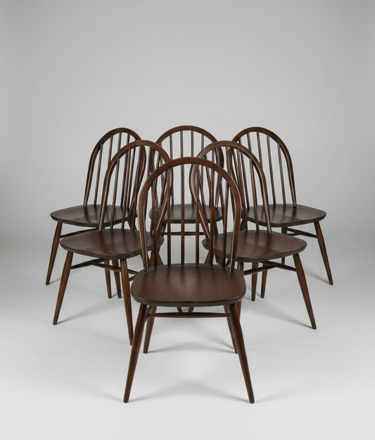 Six dark brown wooden spindle-back dining chairs arranged in a group on a worn reddish-brown floor inside what appears to be a furniture store or warehouse.