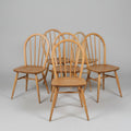 Six wooden dining chairs with spindle backs and seat slats, arranged on a worn red floor in what appears to be a warehouse or furniture showroom.