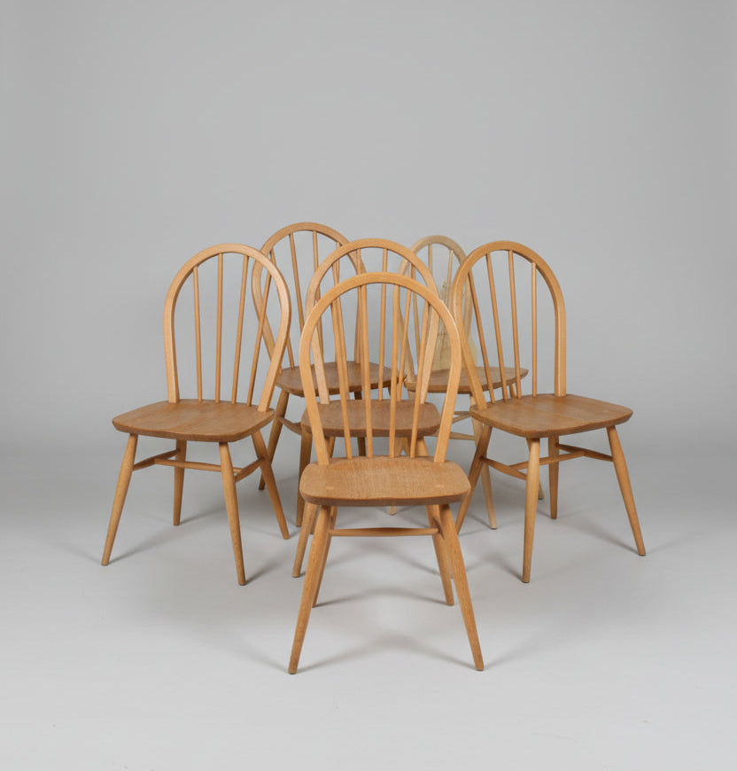 Six wooden dining chairs with spindle backs and seat slats, arranged on a worn red floor in what appears to be a warehouse or furniture showroom.
