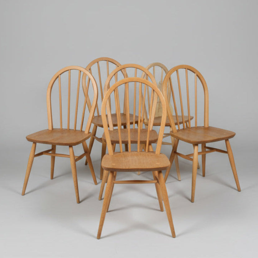 Six wooden dining chairs with spindle backs and seat slats, arranged on a worn red floor in what appears to be a warehouse or furniture showroom.
