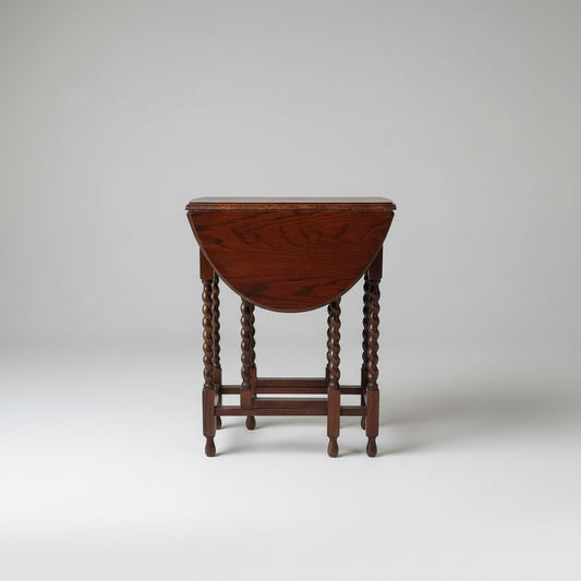 A small antique English oak drop leaf gateleg barley twist table, with visible carved details and a dark wood finish, placed on a woven mat.