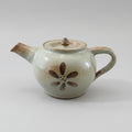 A brown ceramic teapot with a floral pattern on the side, displayed on a wooden surface.