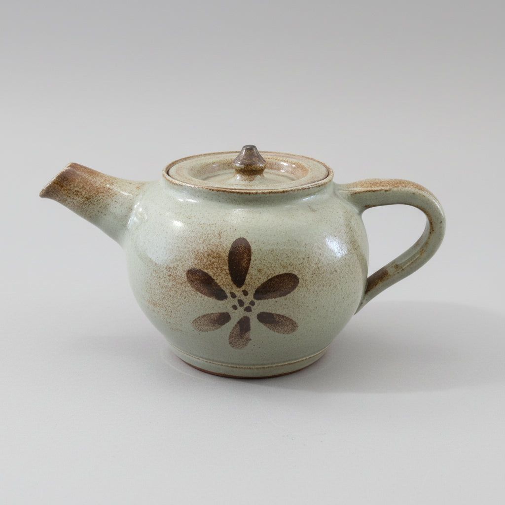A brown ceramic teapot with a floral pattern on the side, displayed on a wooden surface.