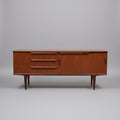 A vintage British teak sideboard from the 1960s with three drawers and a cabinet with folding doors, positioned against a plain background.