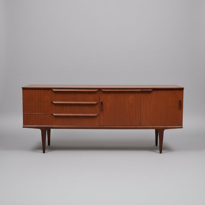 A vintage British teak sideboard from the 1960s with three drawers and a cabinet with folding doors, positioned against a plain background.