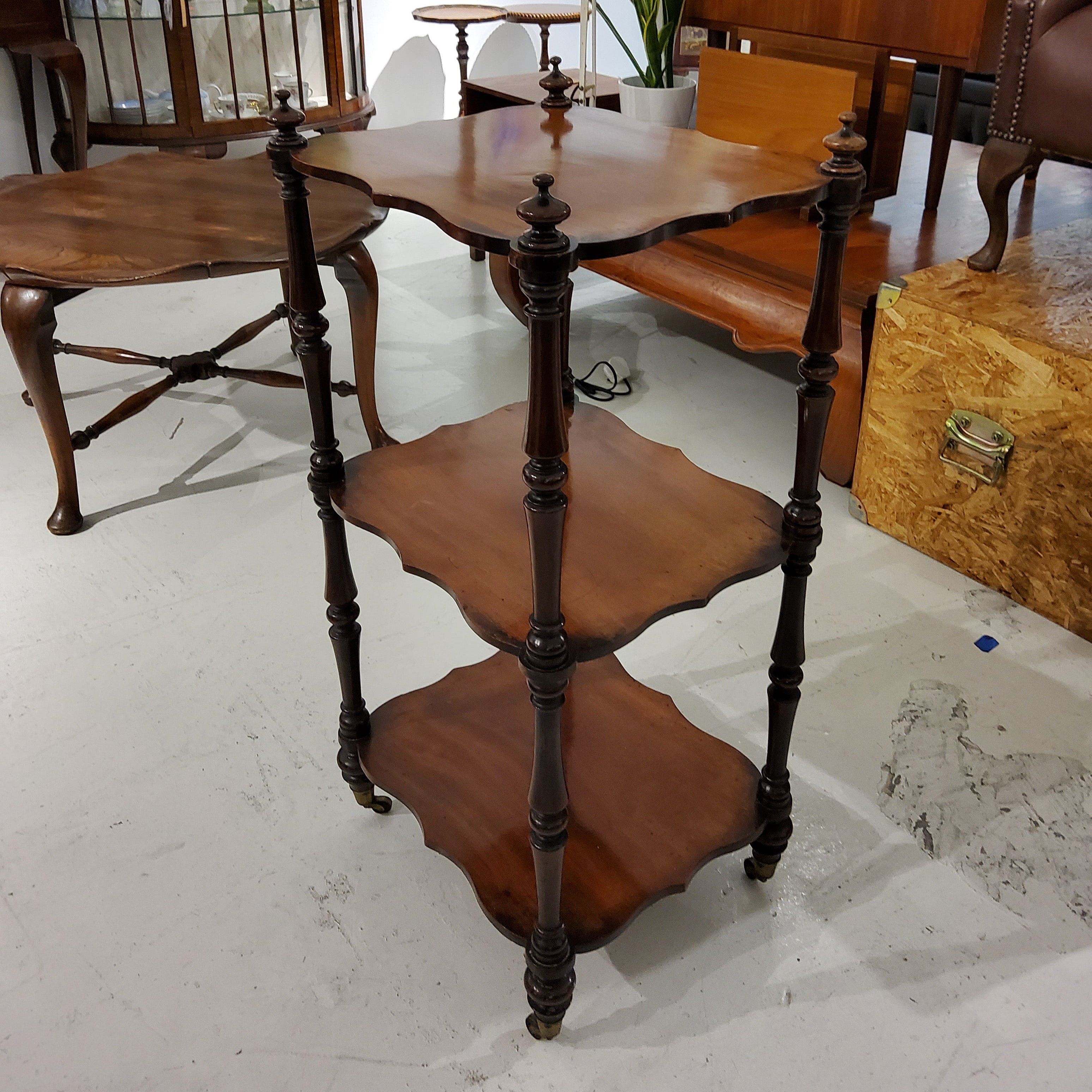 Antique Victorian rosewood whatnot with three serpentine shaped shelves and turned columns, on turned feet with brass cup castors.