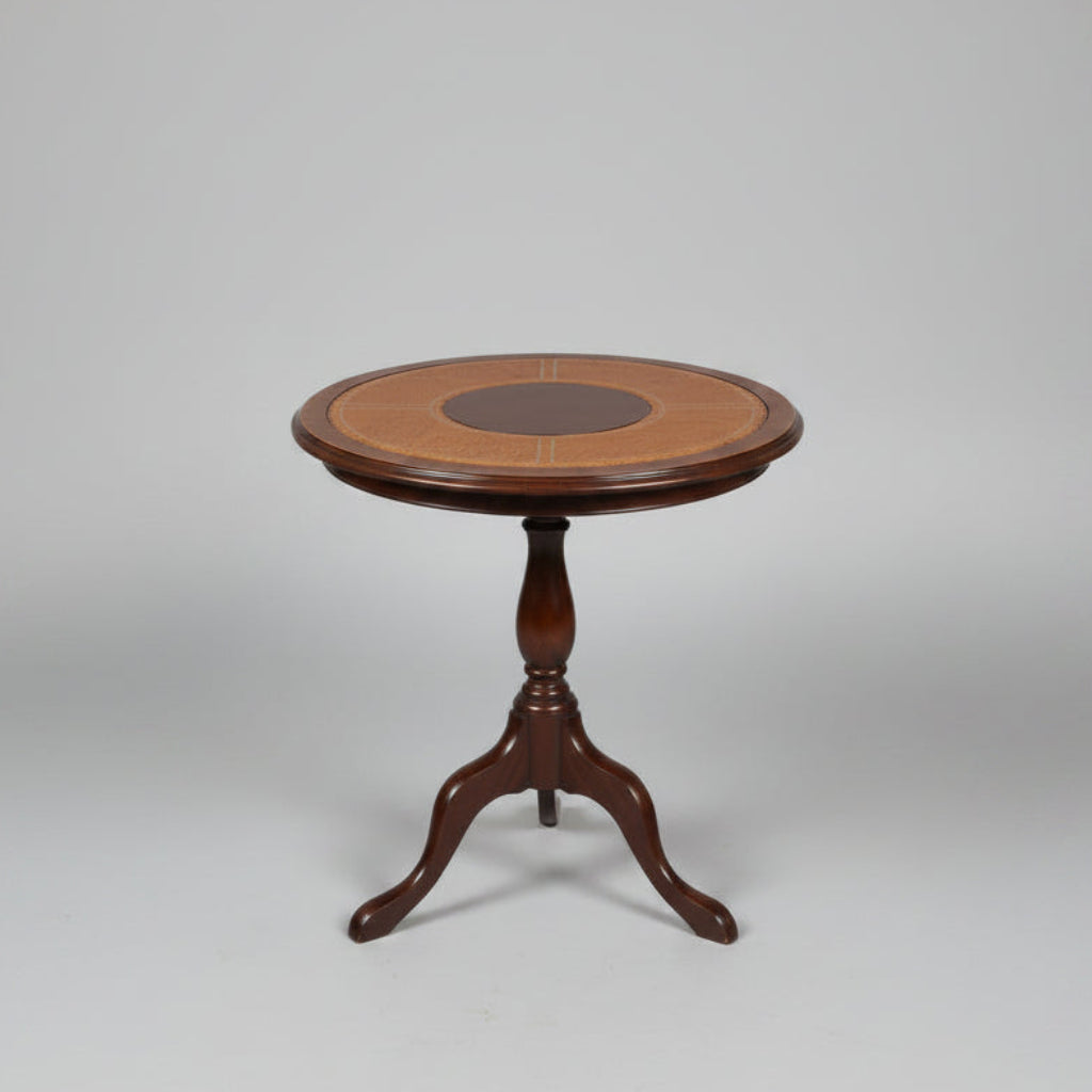 A round wooden side table with a dark metal pedestal base, featuring a light tan woven cane top with a dark brown circular center medallion, set on a distressed red and green floor in front of red stairs.