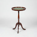 A small round wooden side table with a green top and three legs, photographed in a warehouse or showroom setting on a worn red-brown floor.