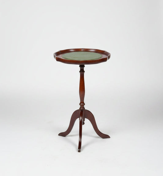 A small round wooden side table with a green top and three legs, photographed in a warehouse or showroom setting on a worn red-brown floor.