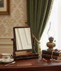 Wooden vanity mirror on a table with a cup, saucer, and oil lamp in a room setting.