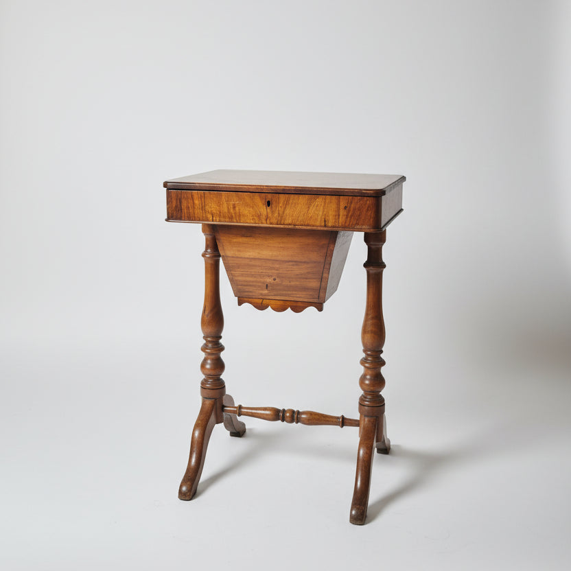 A vintage wooden sewing desk with a   turned legs, positioned in a room with other antique furniture and decorative items.