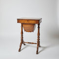 A vintage wooden sewing desk with a   turned legs, positioned in a room with other antique furniture and decorative items.