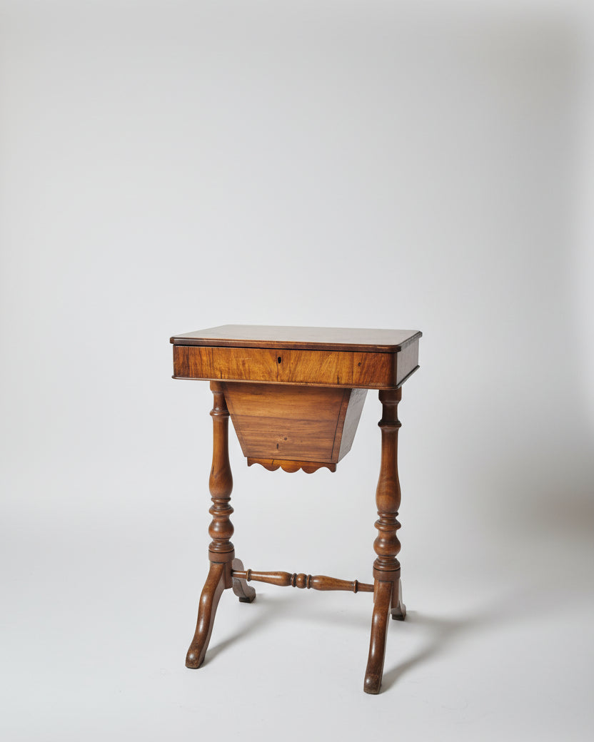 A vintage wooden sewing desk with a   turned legs, positioned in a room with other antique furniture and decorative items.