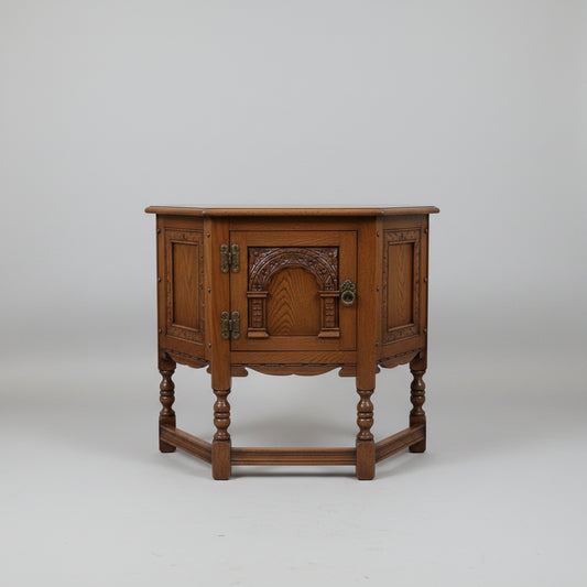An antique-style dark brown wooden side table with carved decorative panels and turned legs, photographed in a furniture showroom.