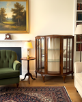 Living room with a green armchair, wooden display cabinet, and a painting on the wall.