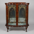 A curved wooden display cabinet with glass doors and ornate gold-toned metal scrollwork, photographed in what appears to be a furniture store or antique shop.