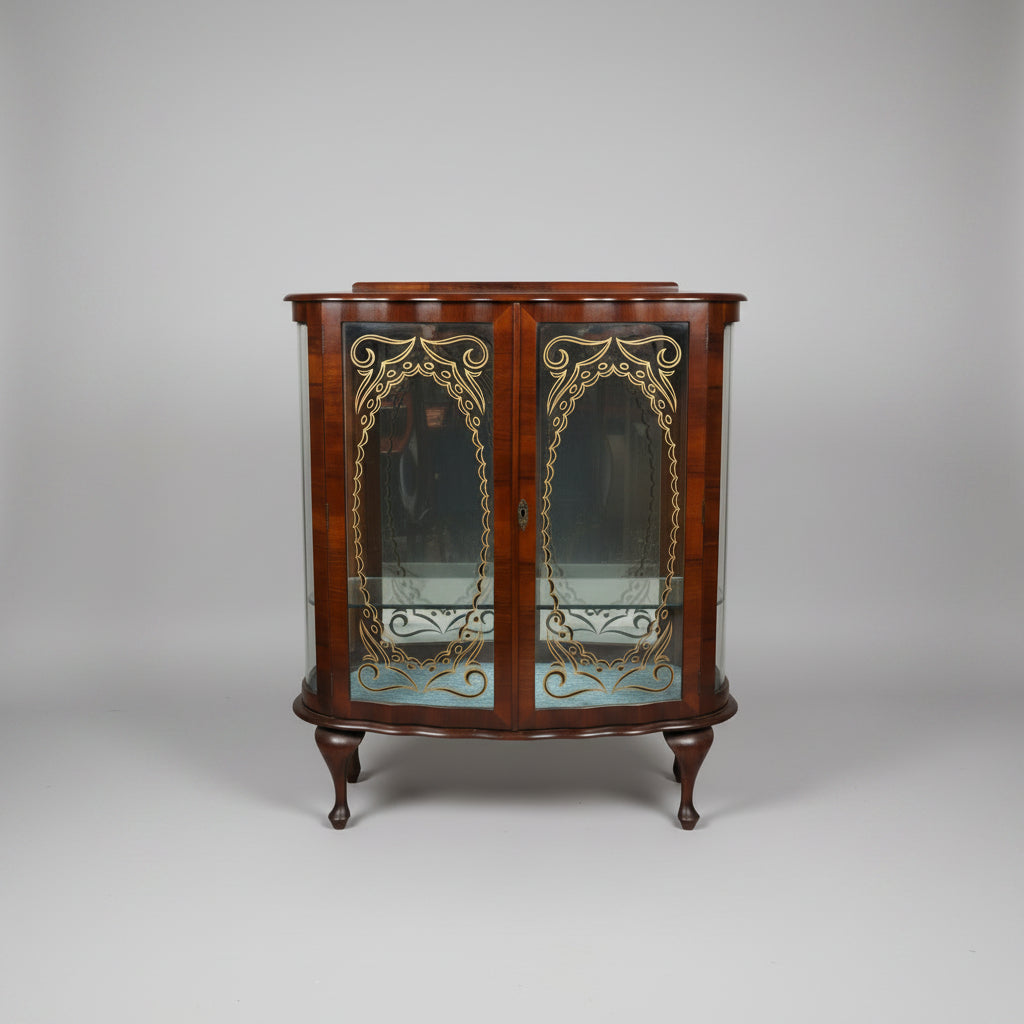 A curved wooden display cabinet with glass doors and ornate gold-toned metal scrollwork, photographed in what appears to be a furniture store or antique shop.