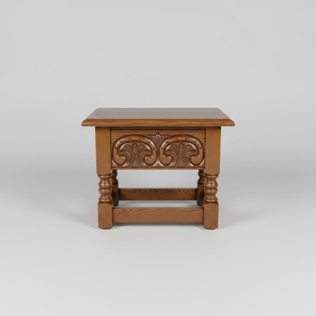A dark brown wooden end table with carved floral details on the front panel and turned legs, photographed in what appears to be a warehouse or furniture store.