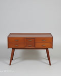 A mid-century modern wooden writing desk with five drawers and brass handles, positioned on a red patterned oriental rug in a room setting.