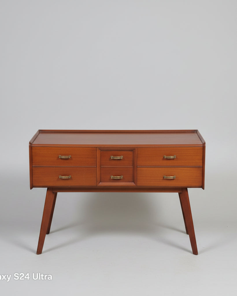A mid-century modern wooden writing desk with five drawers and brass handles, positioned on a red patterned oriental rug in a room setting.