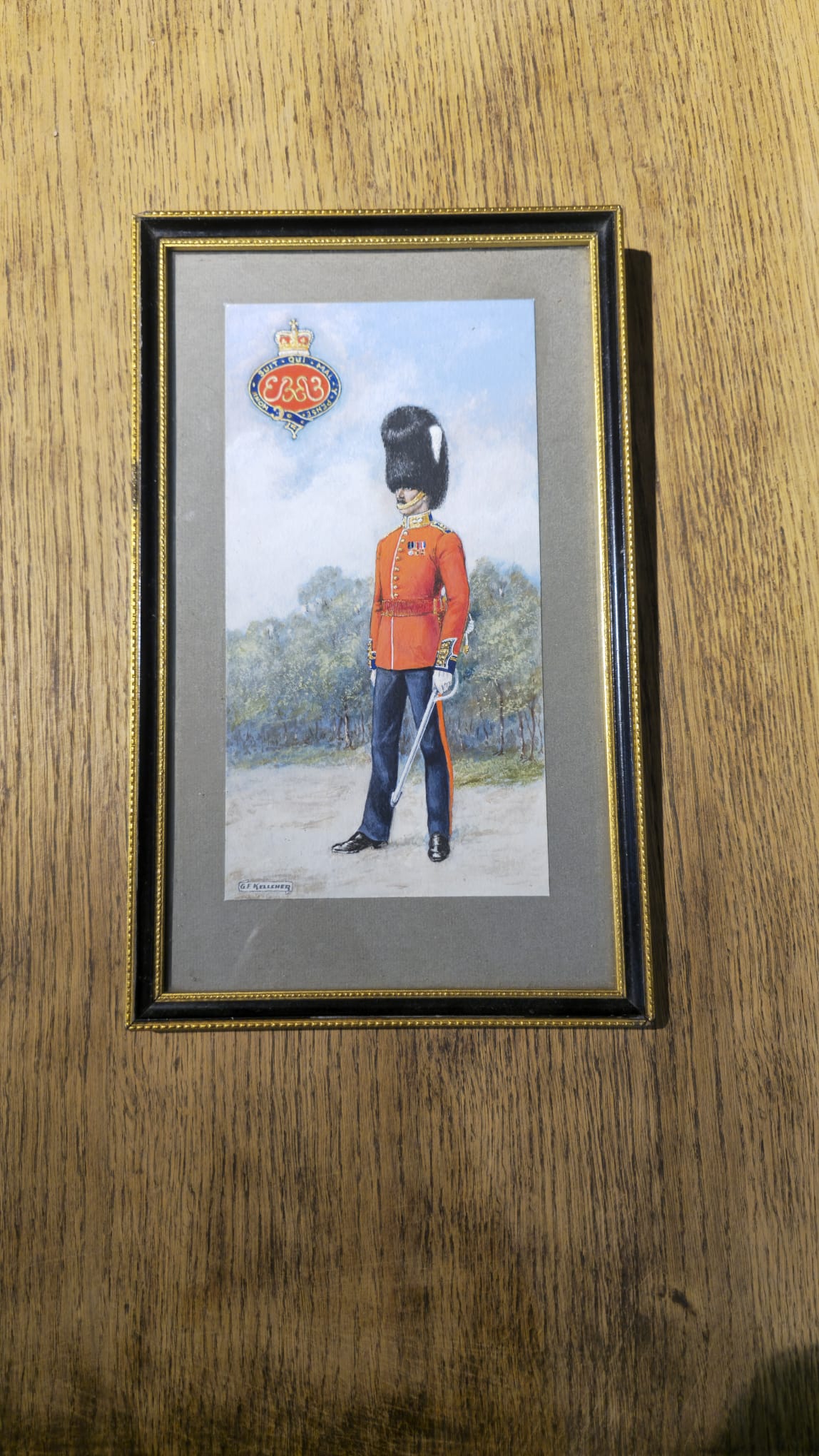 A framed art print depicting a British Royal Guard in red uniform and black bear pelt hat, mounted on a wooden wall.