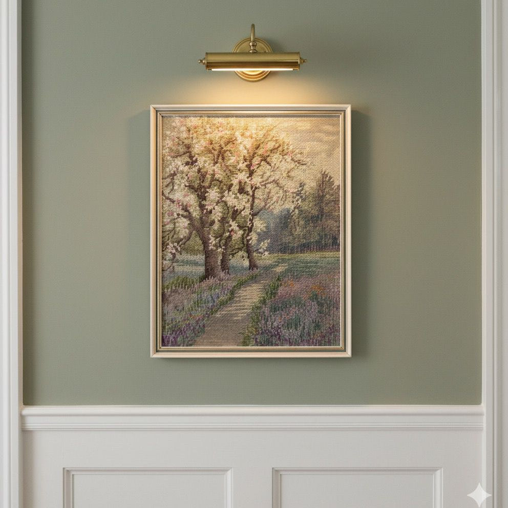 Framed painting of a cherry blossom tree on a green wall with a gold light fixture.