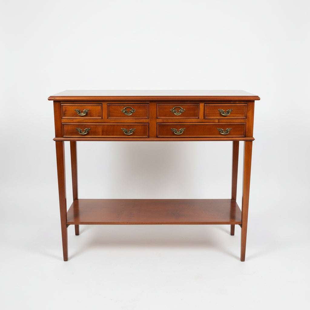 A polished reddish-brown wooden console table with six drawers, ornate brass handles, and an open lower shelf, photographed in a furniture showroom.