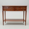 A dark reddish-brown wooden console table with six drawers, brass handles, and an open lower shelf, photographed in a furniture showroom.