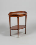 A polished mahogany console table with five drawers, brass handles, and an open lower shelf, shown alongside a matching oval side table on a white background.