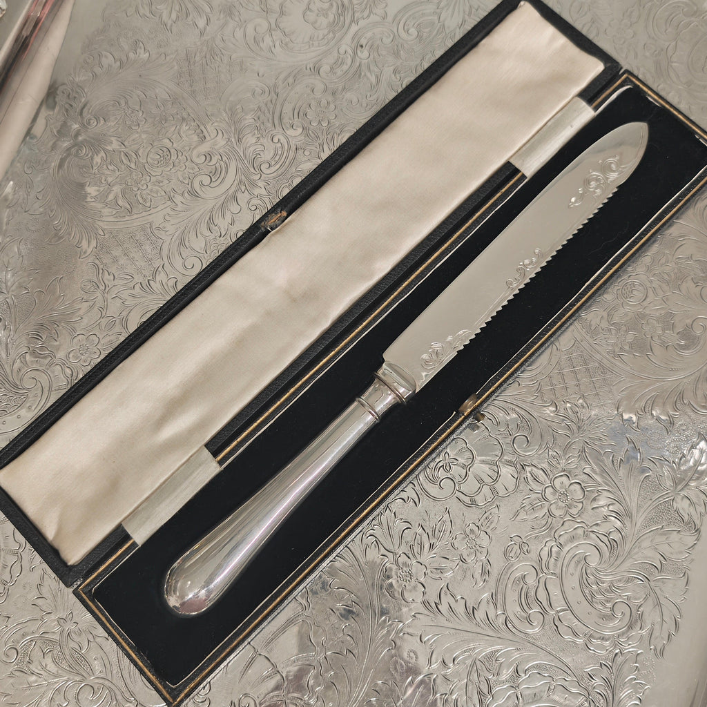 A silver knife and fork set in a black presentation box with a cream fabric lining, placed on an ornate silver tray.