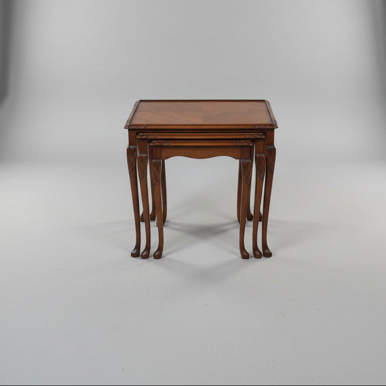 A wooden nesting side table with a geometric inlay top and carved cabriole-style legs, photographed in a furniture showroom with other pieces of furniture visible around it.