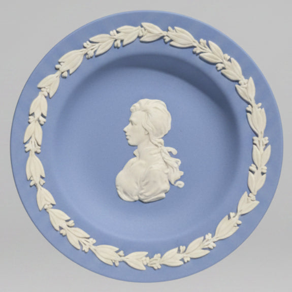 a round blue and white Wedgwood-style ceramic plate with a raised profile bust of a woman surrounded by a leafy border.