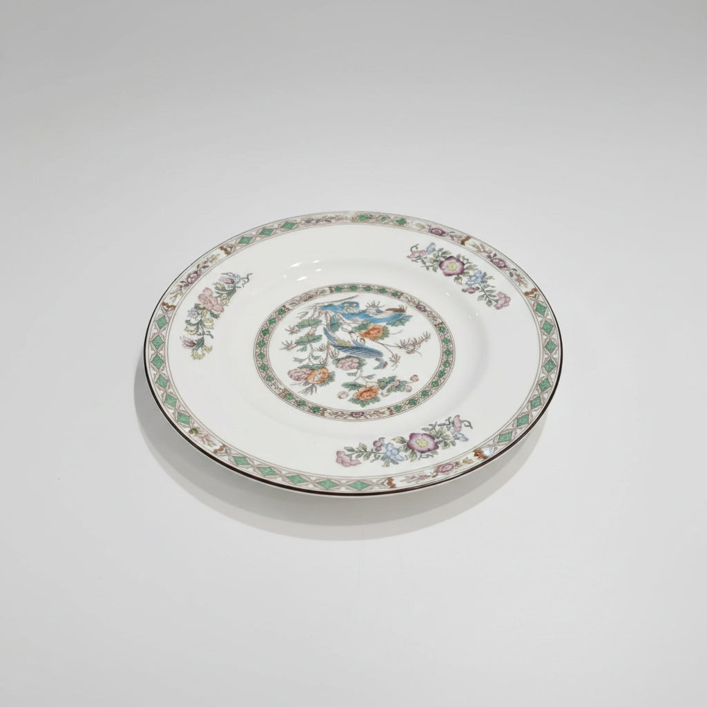 A round white porcelain plate featuring a colorful hand-painted floral border and a central multicolor illustration, displayed on a clean light gray background.