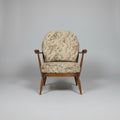 Two vintage wooden armchairs with patterned beige and brown upholstery, shown in a warehouse or showroom setting with a red door and red floor.