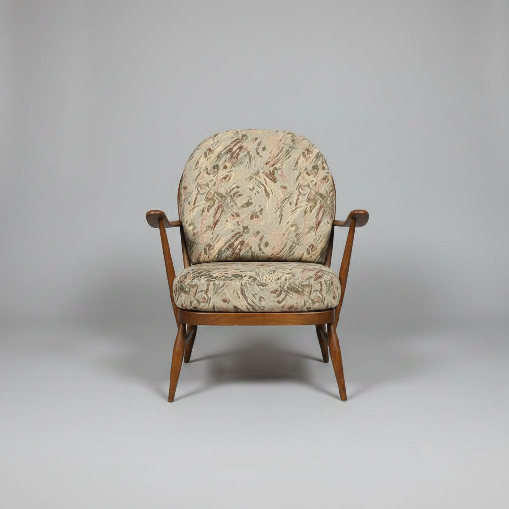 Two vintage wooden armchairs with patterned beige and brown upholstery, shown in a warehouse or showroom setting with a red door and red floor.