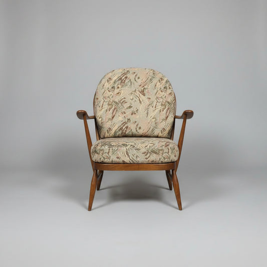 Two vintage wooden armchairs with patterned beige and brown upholstery, shown in a warehouse or showroom setting with a red door and red floor.